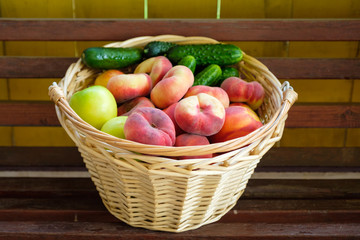 Woven from a vine basket stands on wooden boards filled with fruits from a fresh harvest. Peaches,...