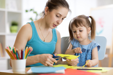 Teacher helping child girl to work with colored paper