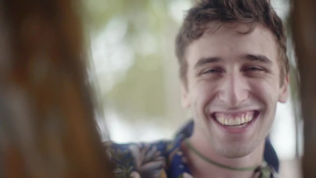 Attractive young Caucasian man smiling into the camera through tree branches. Playing Peek-a-boo