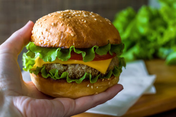 Hamburger in hand. Cheeseburger. The concept of harmful food.
