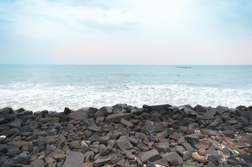 Fototapeta na wymiar Rocky beach with black brown stones and waves dashing into them. Shot at sunset during a cloudy day with the red sky of sunset. This is promenade beach in pondicherry a famous tourist spot