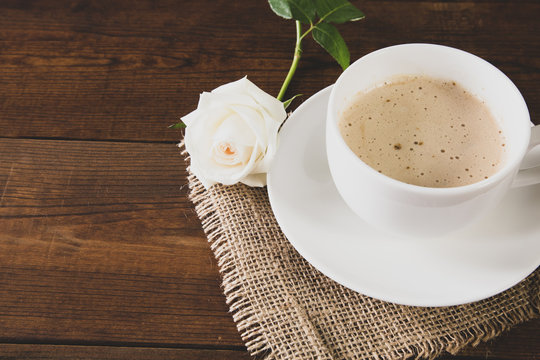 A cup of coffee with beautiful white rose on wooden background