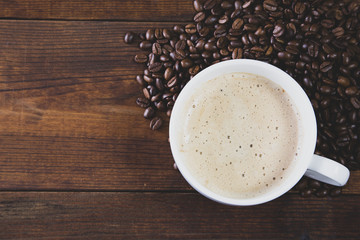 A cup of coffee with coffee beans on wooden background