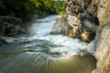 Mountain river with a waterfall flowing between rocky coasts. Over the river trees grow. Taken at sunny spring day at Carpathian mountains. Fast flowing water. Natural background. Freshness feel.