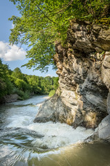 Mountain river with a waterfall flowing between rocky coasts. Over the river trees grow. Taken at sunny spring day at Carpathian mountains. Fast flowing water. Natural background. Freshness feel.