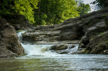 Mountain river with a waterfall flowing between rocky coasts. Over the river trees grow. Taken at sunny spring day at Carpathian mountains. Fast flowing water. Natural background. Freshness feel.