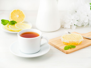 White Cup of tea, honey, honeycomb, lemon on white background. Folk method of treating colds. Side view, selective focus