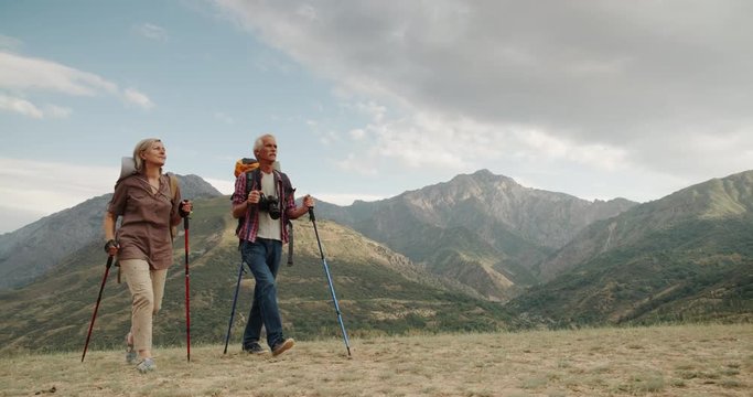Active senior caucasian couple hiking in mountains with backpacks, enjoying their adventure 4k