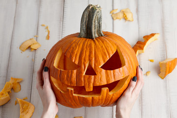 Woman carving big orange pumpkin into jack-o-lantern for Halloween holiday decoration on white...
