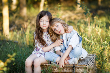 a cute little boy and a girl sitting on a basket outside at sunset an having fun