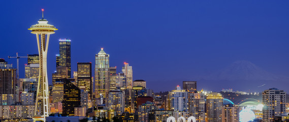 Panoramic beautiful Seattle illuminated skylines downtown during blue hour, view from Kerry Park at Queen Anne Hill. Mount Rainer can be seen from background.