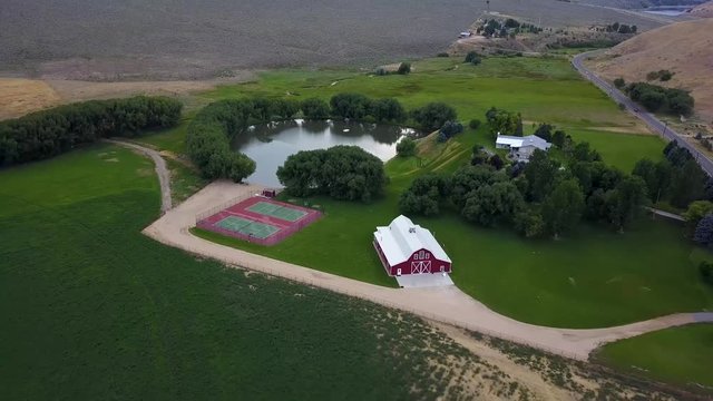 Aerial view of a large farm property with a red barn, tennis courts, pond, and large trees.