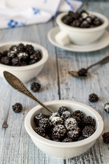 Fresh blackberries with sugar powder in small round cups on an old wooden table. 