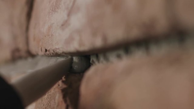 Slow motion handheld closeup of worker filling seam between bricks with mortar from sealant gun