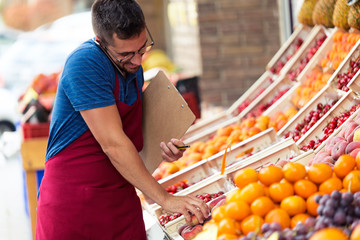 Salesman selecting fresh fruit and talking on the phone in health grocery shop.