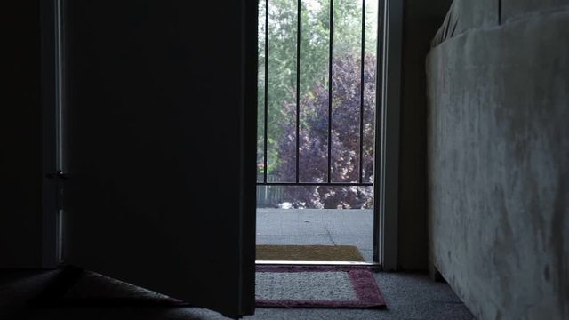 An open door inside of a dark apartment leading to an outdoor hallway at an apartment complex in the summer.