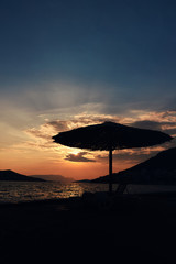 Beach chairs under thatch straw umbrella with sunset in background. Copy space