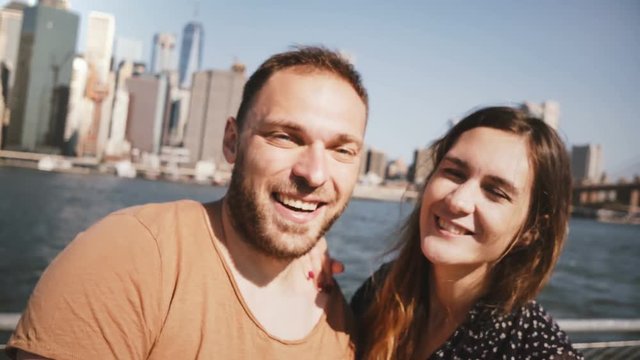 Happy smiling young couple posing for a selfie photo, kissing at famous New York skyline view of Manhattan skyscrapers.