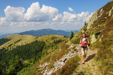 Fototapeta na wymiar A girl with baby in a sling goes at the mountain range. Ukraine. Carpathian mountains
