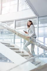 Young smiling businesss woman walking up  the stairs  of a public building  and using a smartphone....