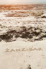 Inscription Zanzibar, Tanzania on the light sand on the beach at low tide