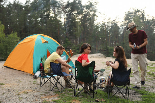 Young people having lunch with sausages near camping tent outdoors