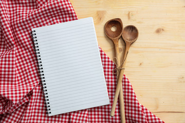 Notebook, kitchen utensils and red tablecloth on wooden table, top view, copy space