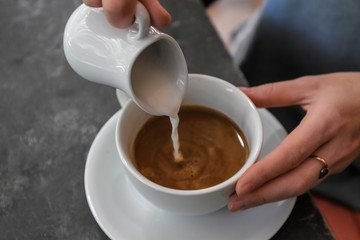 Woman adding milk to fresh aromatic coffee at table, closeup