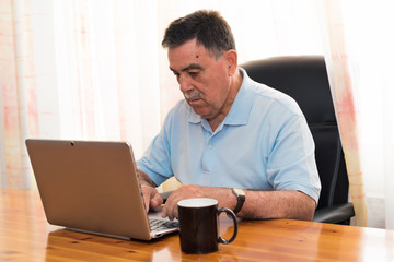 Senior man working on laptop. Neutral expression.