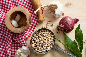 Black eyed beans, herbs and red tablecloth on wooden table, top view