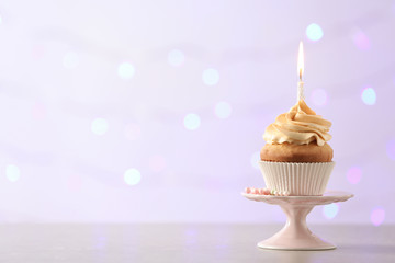 Delicious birthday cupcake with burning candle and space for text on blurred lights background
