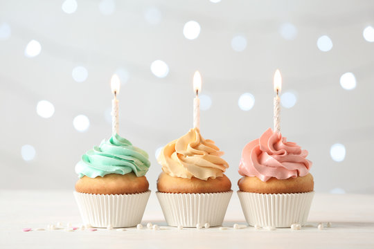 Delicious birthday cupcakes with burning candles on blurred lights background