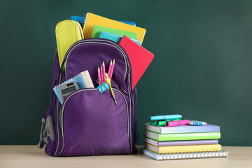 Color backpack and stationery on table near chalkboard with space for text. Ready for school