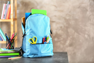 Backpack with school stationery on table indoors