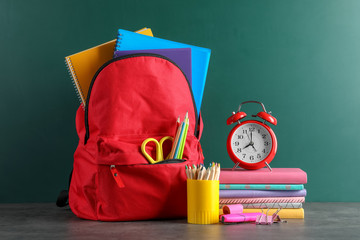 Backpack with school stationery on table against blackboard