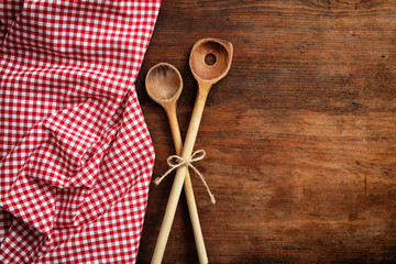Wooden kitchen utensils on red checkered tablecloth on wooden table, top view, copy space