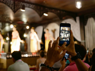 Close up of tourist's hands lifting his phone up to take a photo of beautiful traditional Northern Thai performance / dance