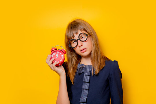 Portrait of a nerd girl in glasses with alarm clock on yellow background