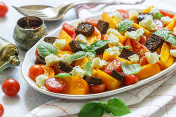 Delicious summer salad of yellow and red tomatoes, croutons, cheese mozzarella,  Basil and olive oil