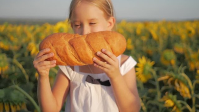 Close up little girl is eating bread in the field of a sunflower. Girl eating bread outdoors.