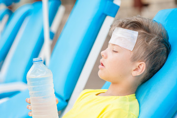Little boy on the beach with a sunstroke holds a bottle of water