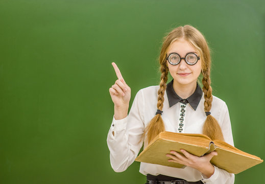 Smiling nerd student girl pointing on empty school board. Space for text