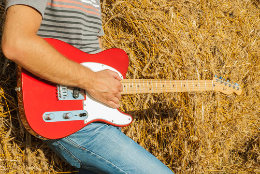 Guitar telecaster in red with a wooden stamp in the hand of a musician background of straw on a sunny summer day