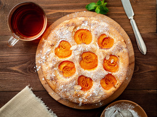 Big Apple pie with apricot, cup of tea, charlotte on dark brown wooden table, top view