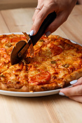 People Hands cutting homemade pizza. Hand slicing a homemade pizza with a cutter on a wooden table