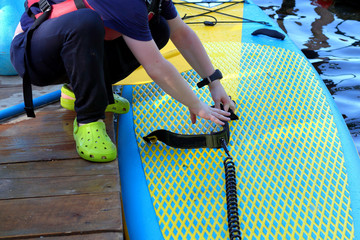 Boy reaches for the hand to leash of blue yellow paddleboard SUP