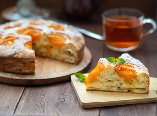Big Apple pie with apricot and piece, cup of tea, charlotte on dark brown wooden table, side view