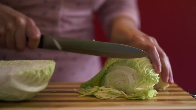 Woman slicing kale on a wooden board with a sharp knife