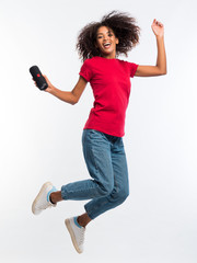 Beautiful african american woman in red t-shirt enjoying and jumping at white background. Modern...