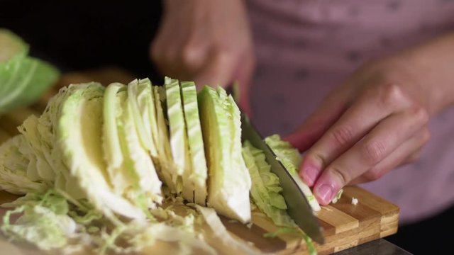 Close-up shot of woman's hands slicing savoy cabbage on a wooden cutting board